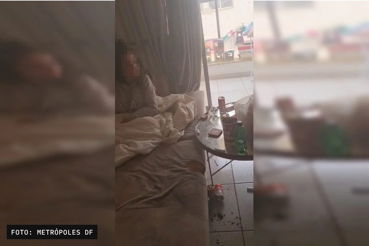 Foto vertical de um ambiente interno, com um sofá ou cama, uma pessoa deitada parcialmente desfocada à esquerda e uma mesa com bebidas e objetos.