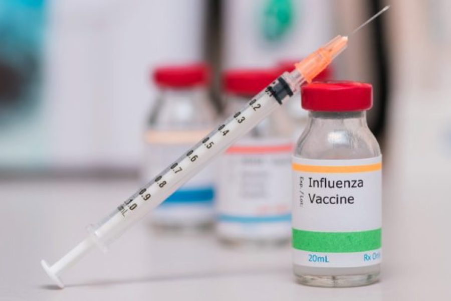 influenza vaccination concept with syringe in vaccine vial and other vials in background